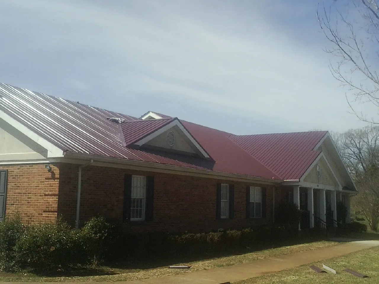 Red metal roof with gabled entries on a long brick building, from a Hail Damage Roof Repair job in Eden